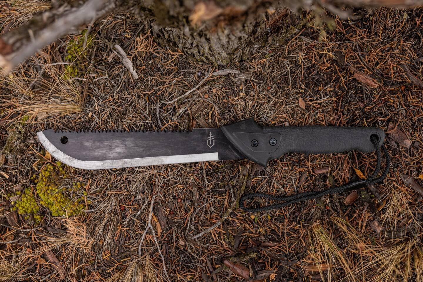 Gerber Gator Machete Dual Junior 50 cm, jossa on kaksipuolisesti teroitettu terä ja ergonominen kahva metsänpohjalla.